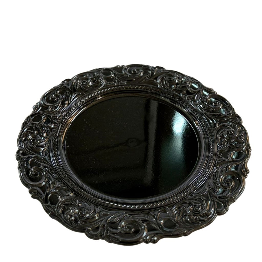 Decorative black round charger plate with intricate patterns on a white background